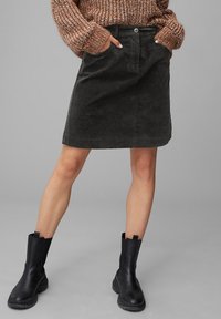 Jupe en velours côtelé noir de forme droite, avec des boutons sur le devant et des poches ; associée à des bottines noires, mettant en valeur un pull en tricot texturé.