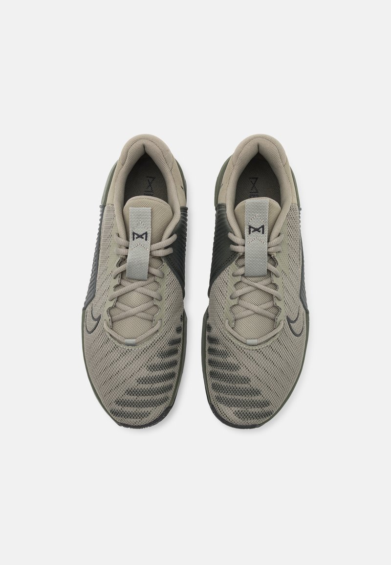 Zapatillas deportivas en tonos beige claro y verde oscuro con parte superior de malla, lados texturizados, cordones grises y un detalle de logo en el lateral. Suela de goma plana.