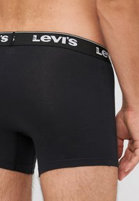 Fekete pamut boxer alsónadrág fekete derékpánttal, amelyen fehér Levi's logó található. Simaság jellemzi, testhezálló fazonnal és combközép hosszúsággal.