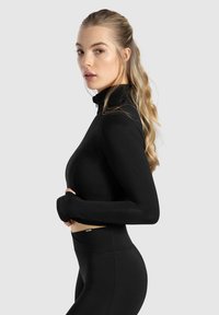 Haut de sport noir à manches longues avec un col haut, design ajusté et trous pour les pouces. Matière lisse et extensible offrant confort et flexibilité.