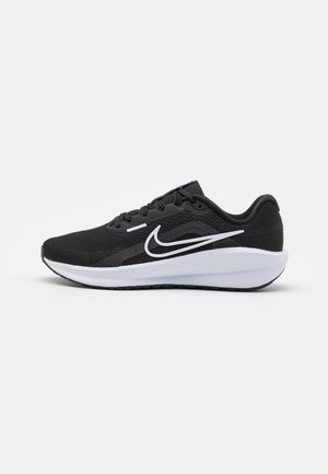 Chaussure de course basse noire avec semelle blanche et logo Nike swoosh blanc sur le côté, présentée sur un fond clair uni.