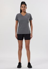 Camiseta deportiva gris con cuello en V y mangas cortas, combinada con shorts negros. La tela parece ligera y tiene una textura suave.