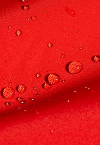 Kropelki wody zbierające się na teksturowanej czerwonej tkaninie, demonstrując odporność lub odpychanie wody.