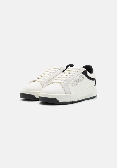Sneaker bianche e grigie con parte superiore in pelle liscia, dettagli in suede testurizzato, linguetta nera sul tallone e suola in gomma con modelli di battistrada.
