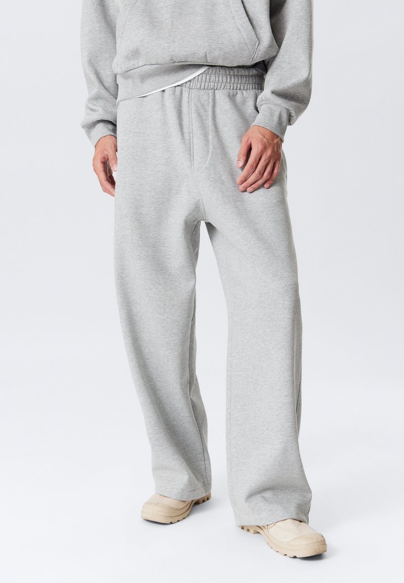 Grå joggingbukser med elastisk talje, vid benstil, blød tekstur og uden synlige mønstre. Kombineret med beige fodtøj.