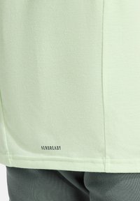 Maglietta atletica Aeroready verde chiaro con una texture liscia. Presenta un logo sul fondo e un design semplice e lineare.