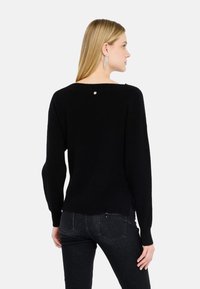 Maglione nero a maglia con maniche lunghe, caratterizzato da un scollo rotondo e un piccolo dettaglio di bottone dorato sul retro. Design testurizzato e dalla vestibilità rilassata.
