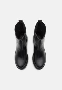 Botas de tobillo de cuero negro con un acabado liso, puntera redondeada y paneles laterales texturizados. Cuenta con tiradores para facilitar el calzado. Suela de goma antideslizante.