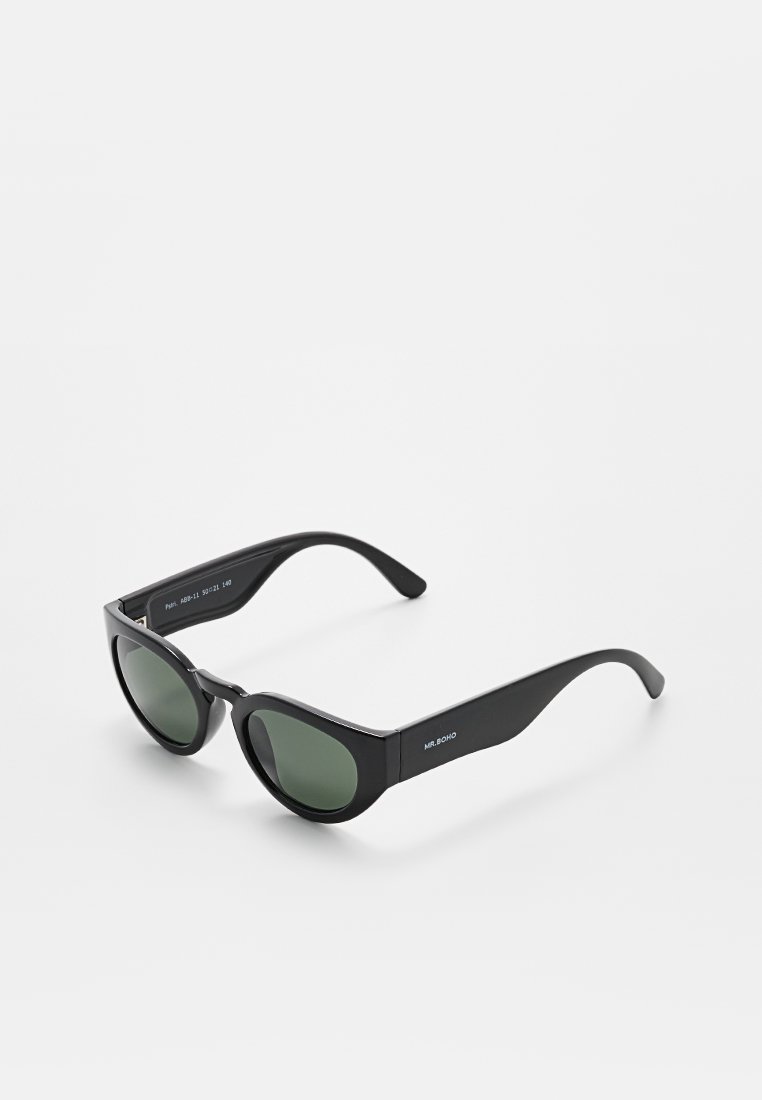 Lunettes de soleil noires avec verres verts, forme angulaire en œil de chat, finition brillante et logo imprimé sur la branche. Monture en plastique léger.