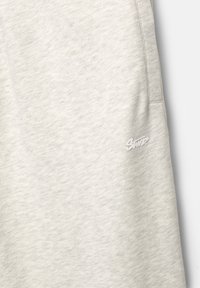 Lichtgrijze sweatpants gemaakt van zachte stof, met een subtiele textuur en een klein logo in het wit op de zijzak.