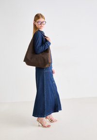 Denimska maksi haljina s dugmadi sprijeda, dugim rukavima i pripijenim strukom; smešna torba; sandale s visokim potpeticama i trakama; pastelnim naočalama.
