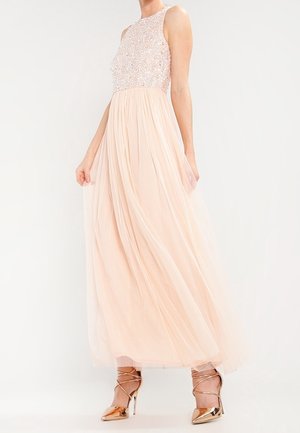 Maxi-jurk met een kralenversierd, mouwloos lijfje en een vloeiende, lichtroze tule rok. Model draagt metallic hoge hakken.