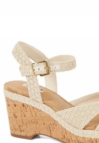 Beige woven platform wedge sandals with cork midsole, adjustable ankle strap secured by a gold buckle, and textured fabric upper.