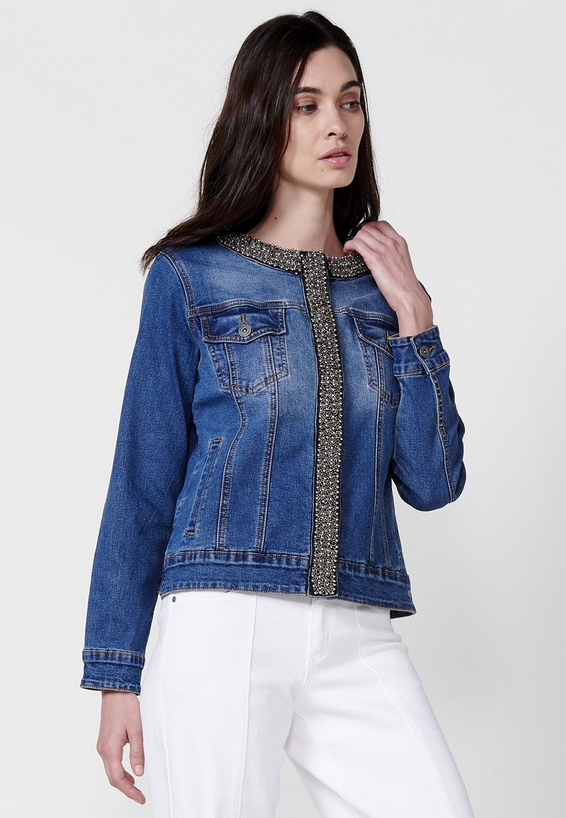 Jeans jakna u plavoj boji, s perlama uz prednji rub, dva džepa na prsima i prilagođenim dizajnom s dugim rukavima.