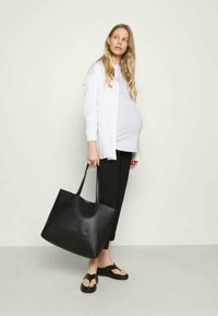 Carteira tote preta em couro com duas alças longas, apresentando uma textura suave e um design espaçoso, complementada por um estilo minimalista.