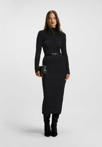 Czarna sukienka z długim rękawem o fakturowanym wzorze, przewiązana w talii paskiem. Połączona z małą czarną torebką i dopasowanymi, czarnymi, wysokimi botkami.