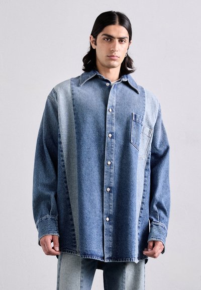 Chemise en denim avec un design bicolore, bleu clair et bleu foncé, dotée d'un bouton sur le devant et d'une poche poitrine unique. Manches longues et coupe décontractée.