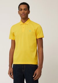 Geel polo shirt in een klassieke pasvorm, korte mouwen, gebreide kraag, drie-knops sluiting, met een klein turquoise logo op de borst.