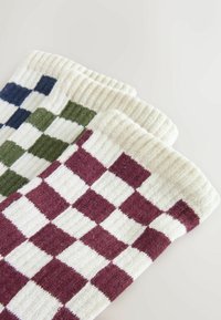 Drie paar geribbelde gebreide sokken met een schaakpatroon in bordeauxrood, olijfgroen en marineblauw op een witte achtergrond.