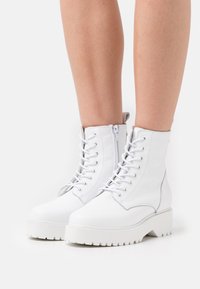 Bottines blanches en cuir avec une finition texturée, dotées d'un laçage à l'avant, d'une fermeture éclair sur le côté et d'une semelle en caoutchouc épaisse.