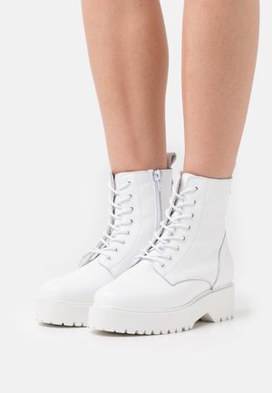 Bílé kožené kotníkové boty s texturovaným povrchem, s předním šněrováním, bočním zipem a robustní gumovou platformou.