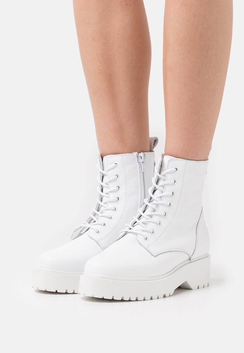 Bottines blanches en cuir avec une finition texturée, dotées d'un laçage à l'avant, d'une fermeture éclair sur le côté et d'une semelle en caoutchouc épaisse.