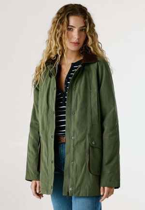 Groene jas tot op de knie van een katoenmix met een bruine corduroy kraag, twee klepzakken en een drukknoopsluiting aan de voorkant. Gestreept shirt eronder.
