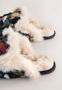 Flauschige Schlupfpantoffeln mit Blumenmusterstoff, cremefarbenem Kunstpelzbesatz und einer strukturierten schwarzen Sohle.