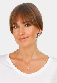 Ezüst nyaklánc teknős medállal, finom lánccal és sima felülettel, fehér v-nyakú pólóval viselve.