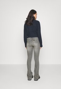 Maglione lavorato a maglia blu scuro abbinato a jeans svasati grigio chiaro, con tasche posteriori e dettagli di cucitura sottili.