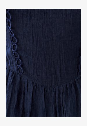 Námornícky modré šaty s textúrovanou látkou, s volánovým lemom a okrúhlou výšivkou pozdĺž výstrihu.