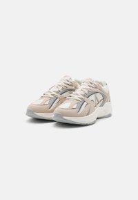 Sneaker mit einer beigefarbenen und grauen Farbgebung, ausgestattet mit Netzpaneelen, Schnürsenkeln und einer gepolsterten Sohle. Leichtes Design mit strukturierten Akzenten.