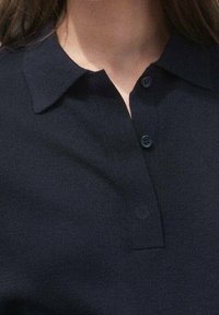 Granatowa koszulka polo z kołnierzykiem, zapinana na dwie guziki, z prążkowaną teksturą i gładkim materiałem. Prosty i klasyczny styl.