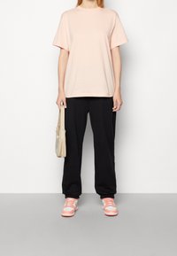 Pink Nike t-shirt, loose fit, short sleeves; black loose sweatpants; pink and white sneakers with a textured design; beige shoulder bag.