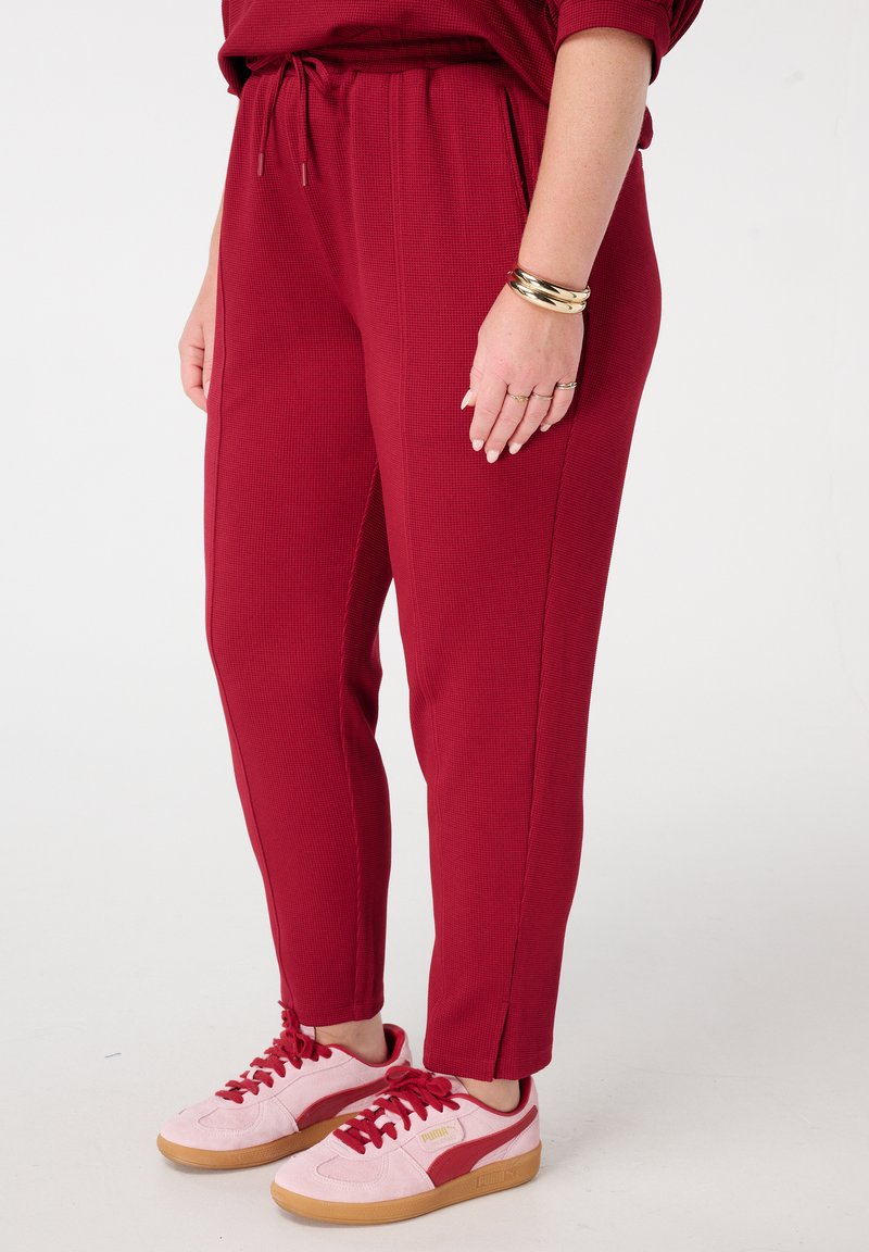 Rode ribgebreide broek met een tailleband met trekkoord, zijzakken en taps toelopende benen, gecombineerd met roze sneakers met een gumrubberen zool.