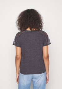Camiseta de color gris oscuro con mangas cortas de encaje, escote redondo y corte relajado. La tela tiene una textura jaspeada.
