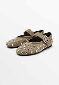 Ballerine in suede taupe con punta arrotondata, decorate con borchie in metallo argentato. Presentano una cinghia con una fibbia metallica per una vestibilità sicura.