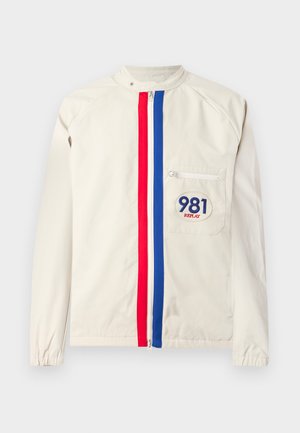 Giacca beige chiaro con strisce verticali rosse e blu, tasca con zip sulla parte anteriore e logo "981 REPLAY" sulla tasca.