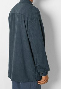 Mörkblå manchesterjacka med vertikal ribbning, långa ärmar och knappmanchetter. Har en avslappnad passform och en enkel design på ryggen.