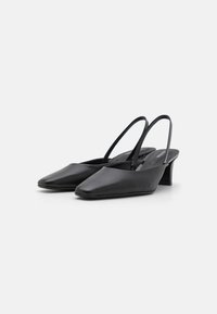 Fekete bőr slingback cipők hegyes orral és alacsony tömbsarkúval. Simább textúrával és minimalista dizájnnal, vékony pántokkal.