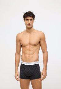 Melni bokseršorti ar ģeometriskiem rakstiem, elastīga josta ar uzrakstu "Calvin Klein", piegulošs dizains, gluda auduma un bez redzamām etikētēm.