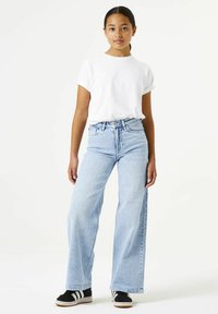 Lichtblauwe jeans met wijde pijpen en een hoge taille, gemaakt van denim. Gecombineerd met een eenvoudige witte katoenen t-shirt en zwarte sneakers.