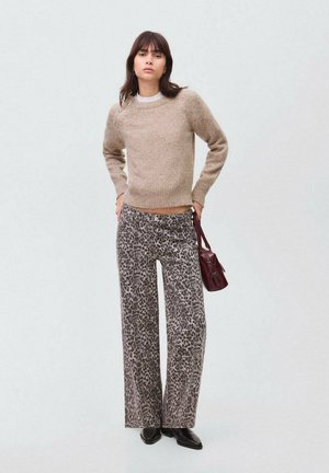 Beige Wollpullover mit rundem Ausschnitt, kombiniert mit grauen weiten Leopard-Print-Hosen. Das Model hält eine burgunderfarbene Handtasche und trägt schwarze Schuhe.