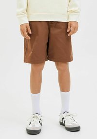 Shorts en coton marron avec une coupe droite, associés à des chaussettes blanches et à des baskets noir et blanc. Le tissu est lisse et léger.