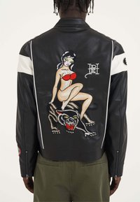 Giacca in pelle nera con arte pin-up ricamata e una pantera. Include bande bianche decorative e una cerniera sulle maniche.