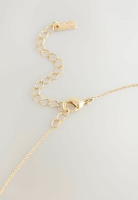 Złota bransoletka z owalnymi ogniwami, zapięciem typu lobster i prostokątną zawieszką z małym kamieniem. Gładka tekstura i błyszczące wykończenie.