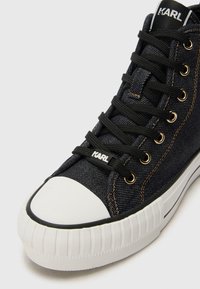 Sneaker alte in denim scuro con punta in gomma bianca e suola texturizzata. Lacci neri e occhielli dorati con il logo "KARL" sulla linguetta.