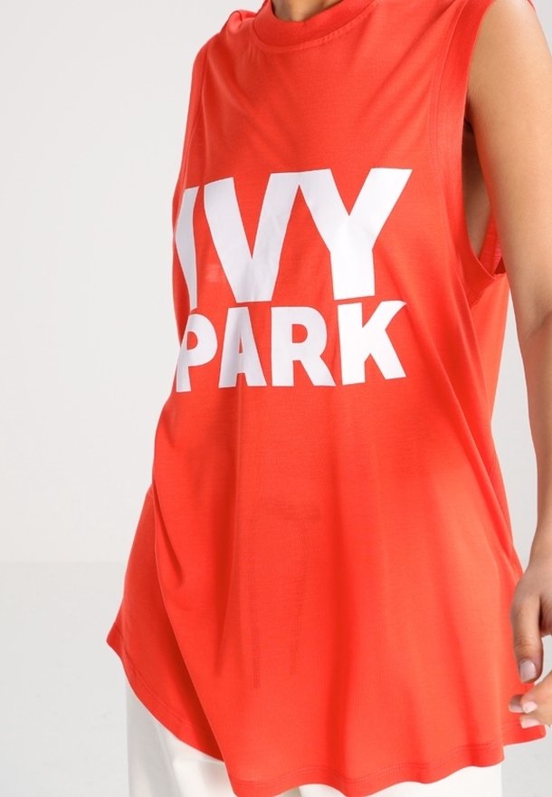 Rød ærmeløs top lavet af letvægtsstof med et fremtrædende hvidt "IVY PARK" logo centreret på forsiden. Normal pasform med rund halsudskæring.