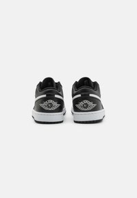 Black leather sneakers with white accents, low-top design, and prominent winged logo embroidered on the heel. Flat rubber sole with tread.