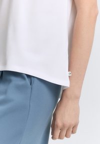 Witte, lichtgewicht top met een gladde textuur, met een rechte zoom en een klein merklabel aan de zijkant, gecombineerd met lichtblauwe broek.